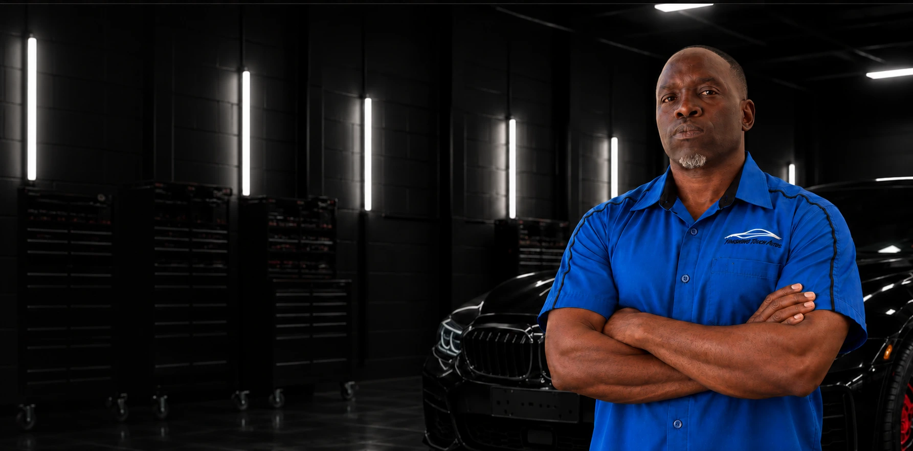 Derrick in his blue Finishing Touch Autos work shirt, standing with his arms crossed in the garage